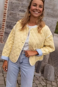 Detail of light yellow quilted jacket featuring white trim and blue striped cuff lining