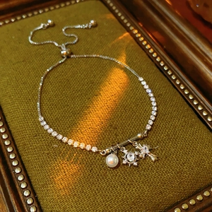 Detail of silver pearl bracelet with zircon cross and star charms on green velvet
