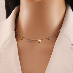 Detail view of a gold chain necklace with turquoise beads and evil eye pendant on model