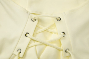 Close-up of yellow knit top featuring silver metal eyelets and cross-laced straps