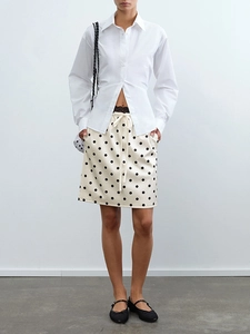 Detail eines schwarz-weißen Polka-Dot-Midirocks kombiniert mit weißem Langarmhemd