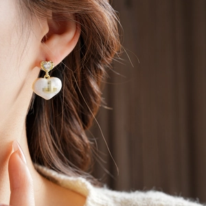 Close-up of gold heart earrings with sparkling crystals and white enamel on a model