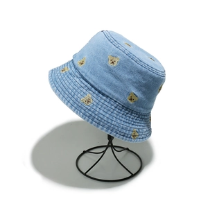 Detail of light blue denim bucket hat with yellow bear embroidery on a metal stand