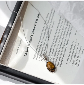 Macro shot of oval tiger eye stone pendant with silver snake chain on decorative paper