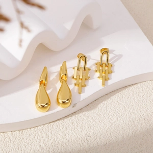 Golden geometric water drop and bar stud earrings set on a minimalist white stone background