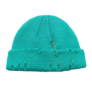 Close-up of teal knit beanie featuring distressed holes with silver pins and metal rings