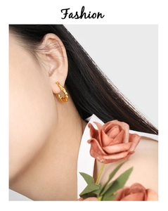 Detail of gold twisted rope hoop earring worn by model with a vintage rose background