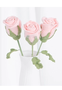 Close-up of pink crocheted yarn roses with green leaves in a white ceramic vase