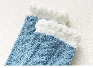 Detailed close-up of blue coral fleece socks with soft white plush cuffs on a cozy blanket