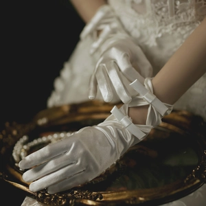 Close-up of white bridal satin gloves with delicate wrist bow and lace-up details