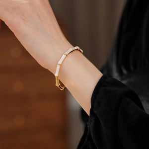 Detail showing gold-plated bamboo joint bangle with white enamel accents on model's wrist
