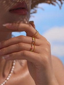Close-up of gold open rings with colorful enamel dots worn against a summer background