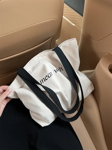 Detail of a minimalist canvas tote bag with letter print on a leather car seat