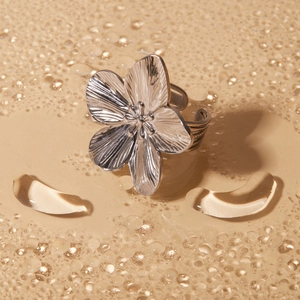 Vue macro d'une bague fleur argentée texturée sur fond beige avec des gouttes