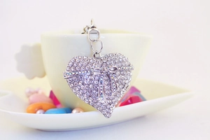 Sparkling crystal heart keychain with a rhinestone bow leaning against a tea cup