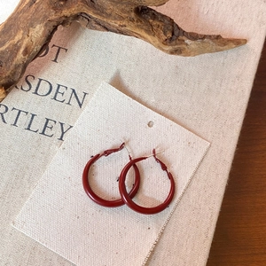 Detail of red geometric hoop earrings on a beige card with a rustic branch and book