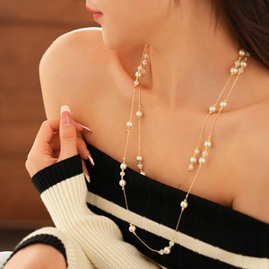 Detail of a double-layered gold necklace with white faux pearls on model neck