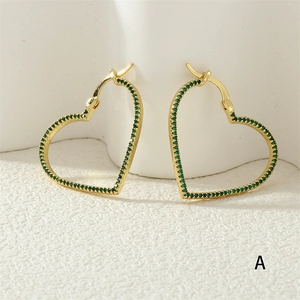 Detail of gold heart earrings featuring sparkling green pavé-set crystals on white background