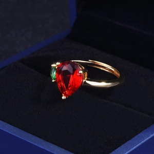 Macro shot of 18k gold open ring with large pear-shaped ruby and green side stone in a box