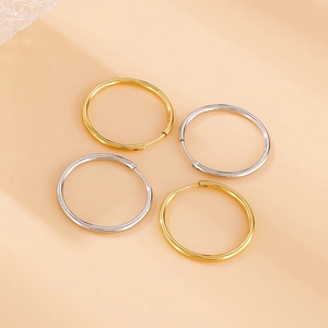 Detailed view of classic gold and silver stainless steel hoop earrings on beige background
