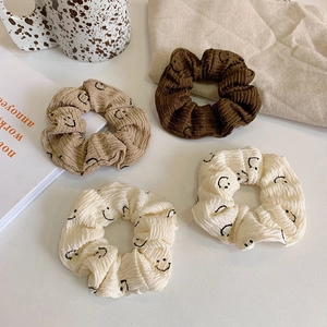 Set of four smiling face fabric hair scrunchies in beige and brown on white surface