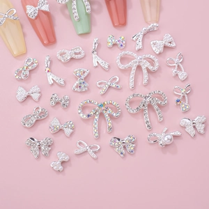 Sparkling silver bow nail art charms set with crystals and pearls on pink background