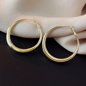 Macro detail of high-polish gold hoop earrings resting on pink silk and black leather