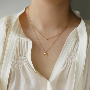 Close-up of double-layer gold necklace with green gemstone and moon pendant on model