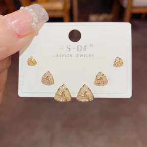 Close-up of three pairs of golden geometric triangle stud earrings with shiny cubic zirconia