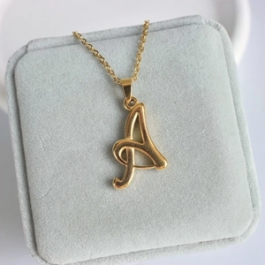 Détail d'un pendentif monogramme 'A' en or 18 carats dans un écrin en velours gris doux