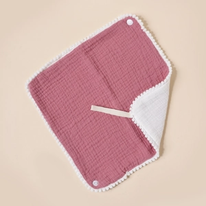 Close-up of muslin cotton baby bib featuring white pom pom trim and snap button detail