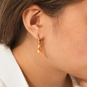 Detail of gold hoop earring with flower, pearl, and coral charms on a model