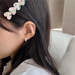 Detail showing elegant double pearl earrings and marble heart hair clip worn on a model