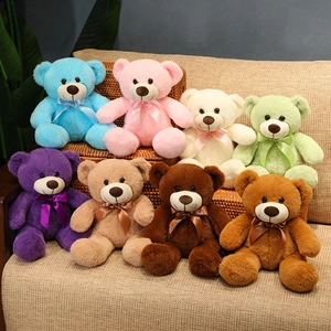 Set of eight colorful plush teddy bears with ribbon bows arranged on a soft beige sofa