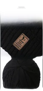 Detailed macro view of black ribbed knit beanie with brown leather logo and seam construction