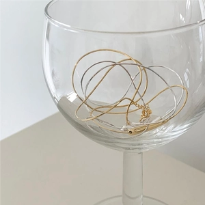 Detailed view of minimalist gold and silver snake chains draped inside a glass cup