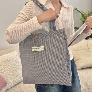 Detail of checkered canvas tote bag featuring a smiling patch and orange button accent