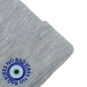 Detailed close-up of grey knit beanie with No Bad Vibes evil eye embroidered patch