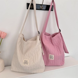 Detail view of striped pleated canvas tote bags in cream and pink with brand label