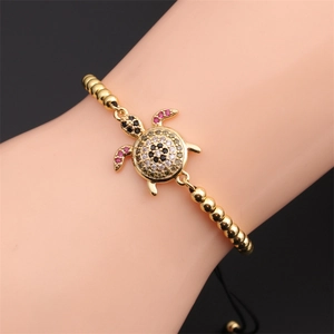 Wrist shot of golden sea turtle bracelet featuring colorful zircon inlay and cord