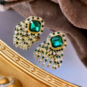 Détail de boucles d'oreilles dorées vintage avec émeraude carrée et pompons de diamants