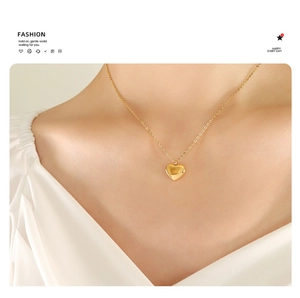 Detail shot of a polished golden heart pendant necklace worn on a white V-neck top