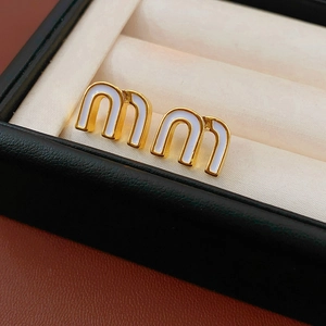 Detail shot of golden letter M earrings with white enamel finish in a jewelry display box