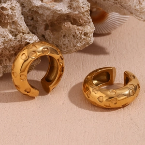 Detailed close-up of gold-plated heart engraved ear cuffs on a natural coral stone