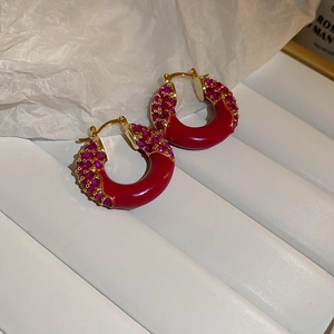 Macro detail of golden C-shaped earrings with magenta zircons and red enamel inlay