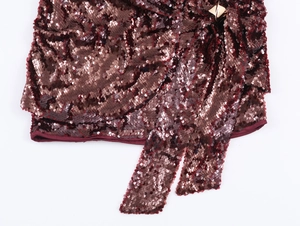 Dettaglio dell'abito con paillettes bordeaux con fibbia dorata e nastro elegante