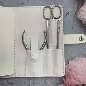 Detailed view of white leather manicure kit with 4 metal tools on marble background