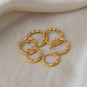 Set of 6 gold twist textured stainless steel hoop earrings on beige fabric background
