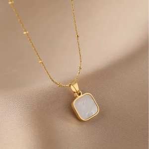 Minimalist gold necklace with white square shell pendant on champagne silk background