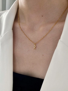Detail of gold chain necklace with a zircon-inlaid letter R pendant worn by model